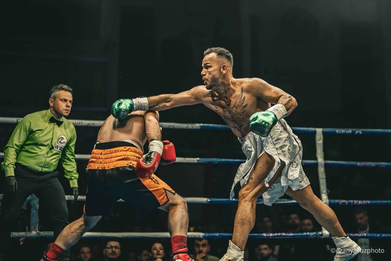 A boxer lands a straight punch as the referee watches from the corner.